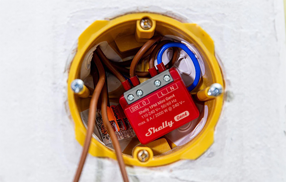A small red controller mounted inside a yellow electrical box in a wall along with wires.