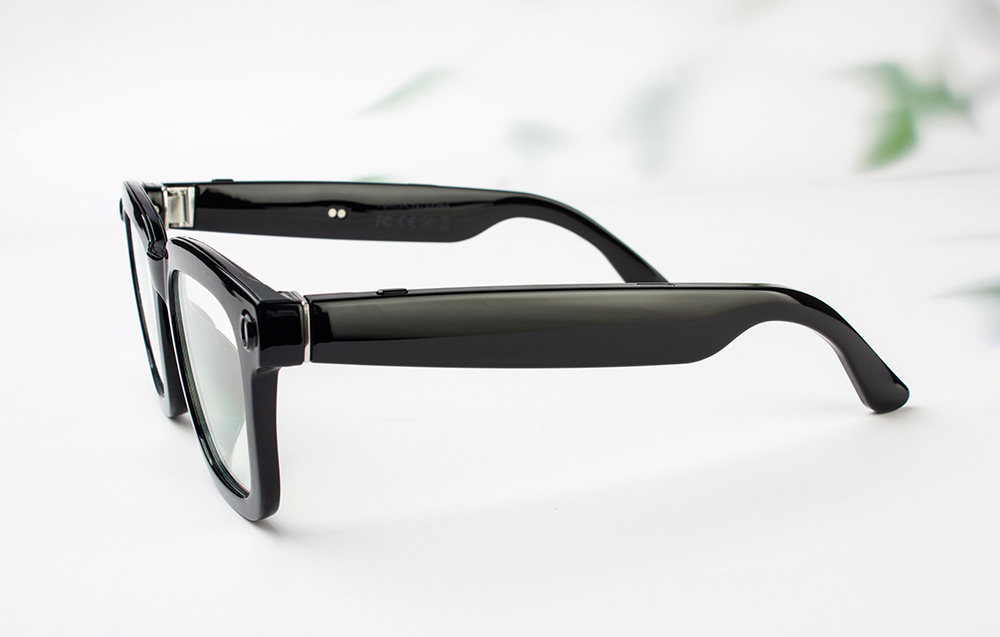 Close-up of the side of black, shiny smart glasses frames lying on a light background.