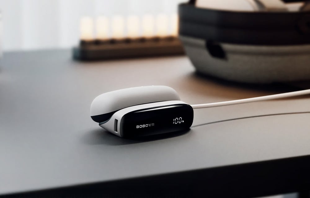 BoboVR PD100 module with cable connected on a desk, display shows 100% charge level