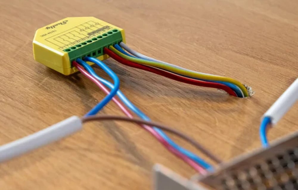 Yellow Shelly LED strip controller with connected wires on a wooden desk