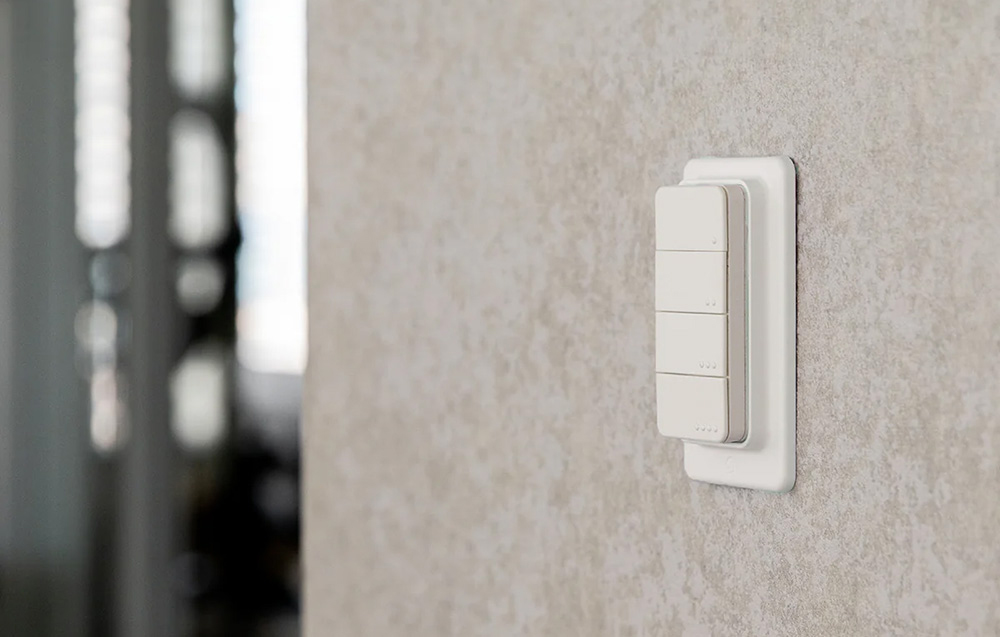 Smart remote control with 4 buttons attached to a gray wall