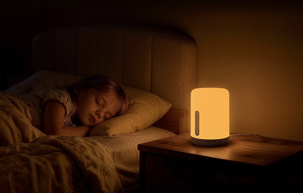 A child sleeping in bed, next to which a nightlight casts a warm glow on a wooden nightstand