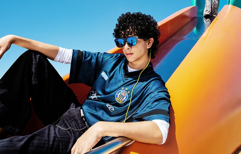 A person wearing sunglasses with blue lenses and a blue sports T-shirt is sitting on an orange slide