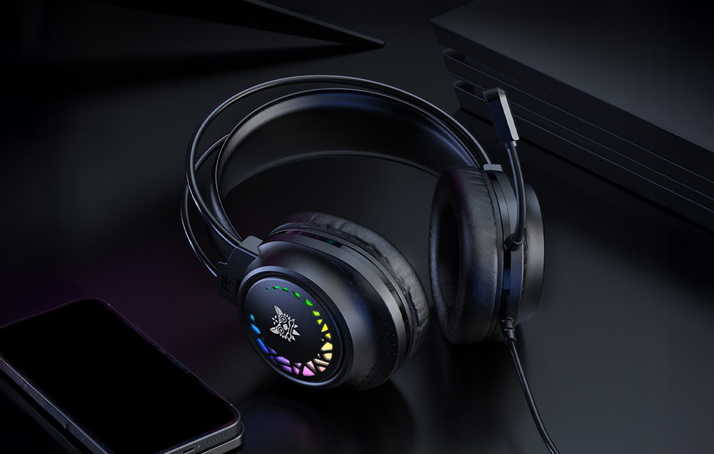 Black over-ear headphones with colored backlight lying on a dark countertop next to a smartphone