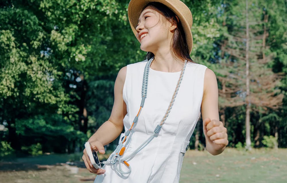 Woman in white dress and hat wears PGYTECH neck strap