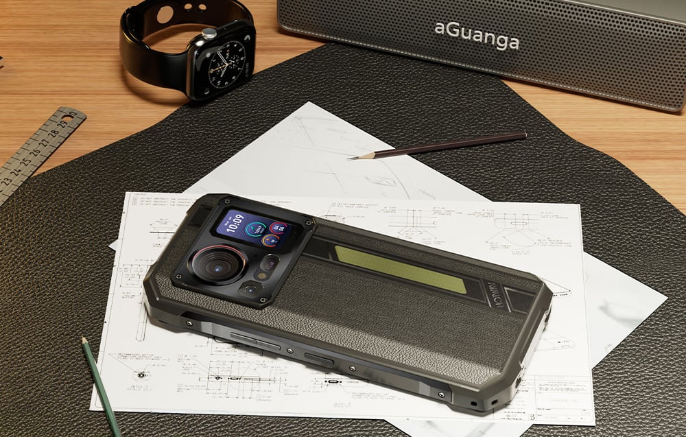 A rugged smartphone lying on architectural plans next to a pencil, smartwatch, and wireless speaker.