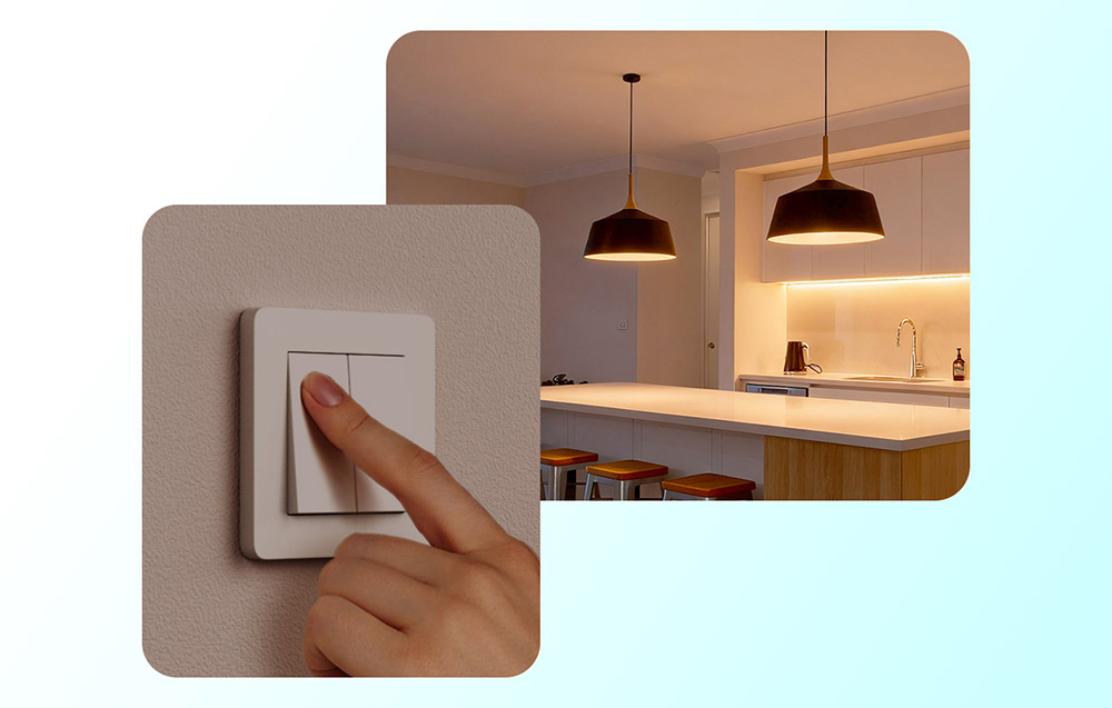 A hand pressing a white light switch on a wall, with a view of a modern kitchen lit by pendant lamps in the background