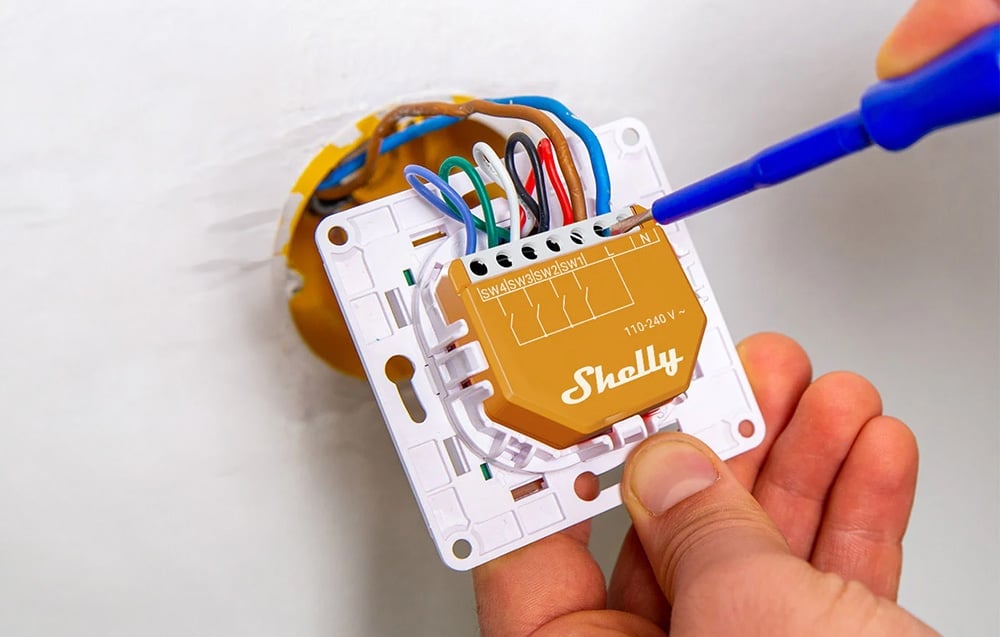 Hands using a screwdriver to install wires in the orange Shelly module