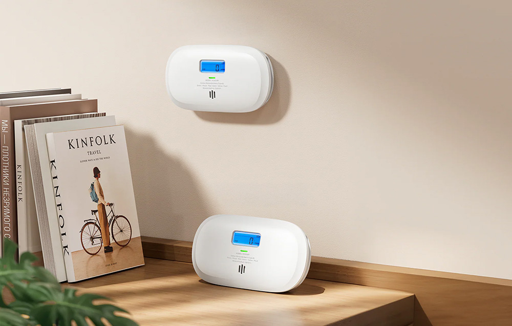 Two X-Sense carbon monoxide detectors - one on the wall, the other on a desk next to books