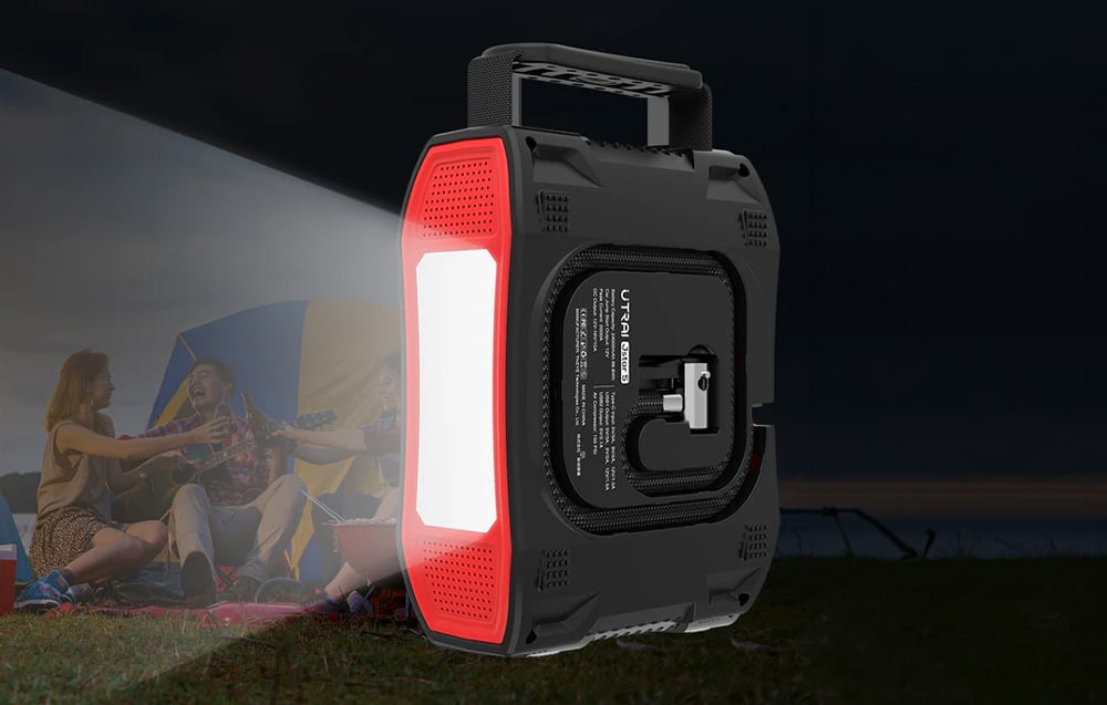 A portable jump starter with a powerful flashlight turned on, illuminating a campsite at night.
