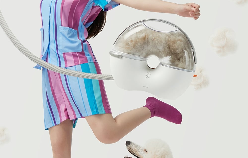 A person in a striped dress holds a vacuum cleaner hose with a transparent chamber that has dog hair in it