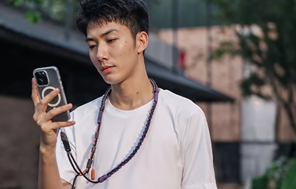 A man in a white shirt uses his smartphone and wears a PGYTECH strap around his neck