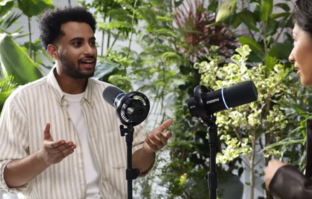 A woman and a man talking into Maono microphones against a backdrop of green plants