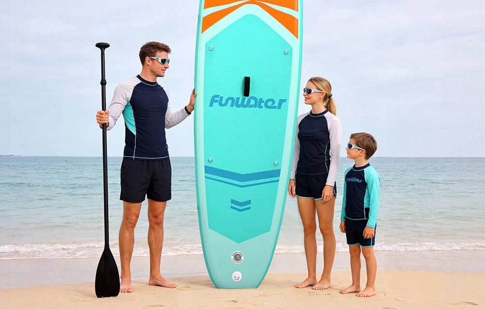 A family with a child stands on the beach, a man holds a surfboard and a paddle in his hands
