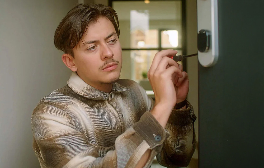 Young man programs smart lock on green door by pressing touch sensor
