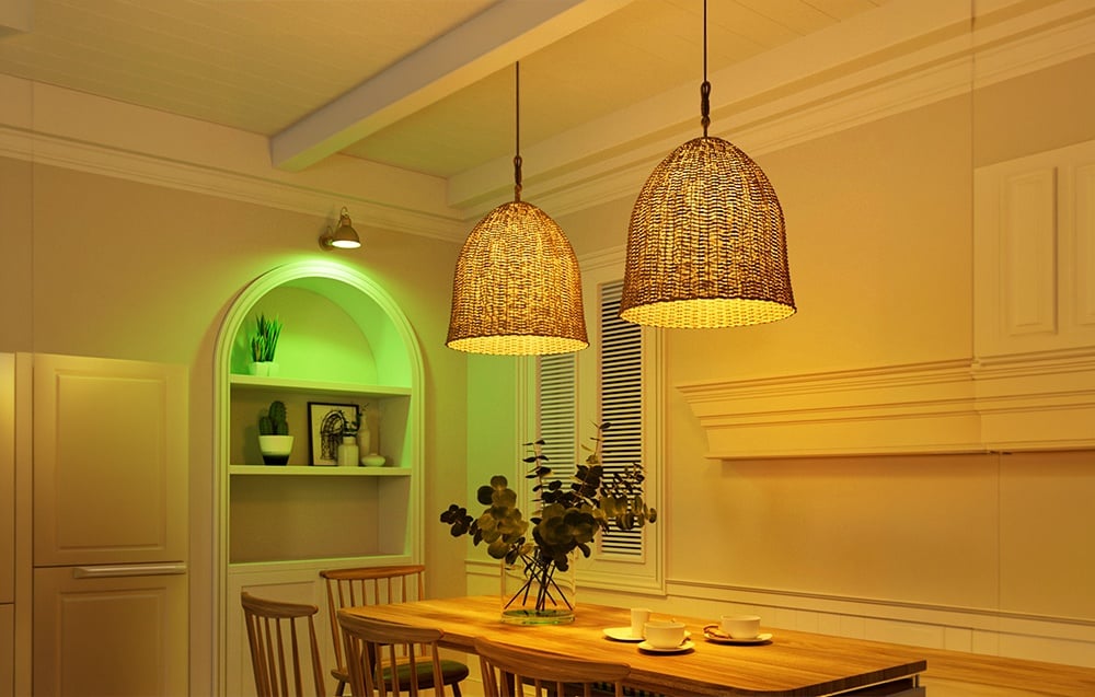 Two woven pendant lamps hanging over a wooden dining table in a room with warm yellow and green lighting.