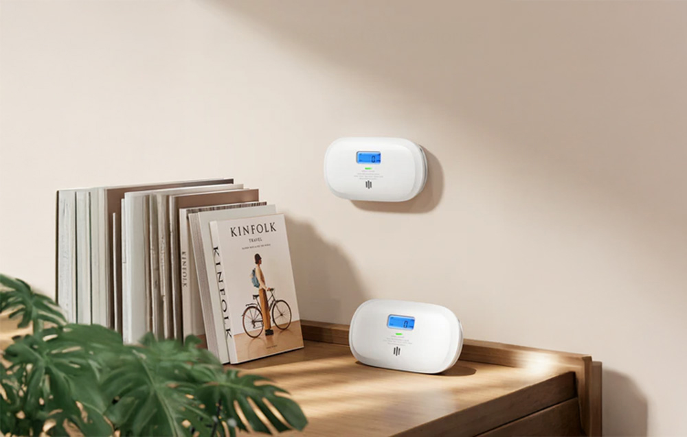 Two carbon monoxide detectors - one mounted on the wall, the other set on the dresser next to the books