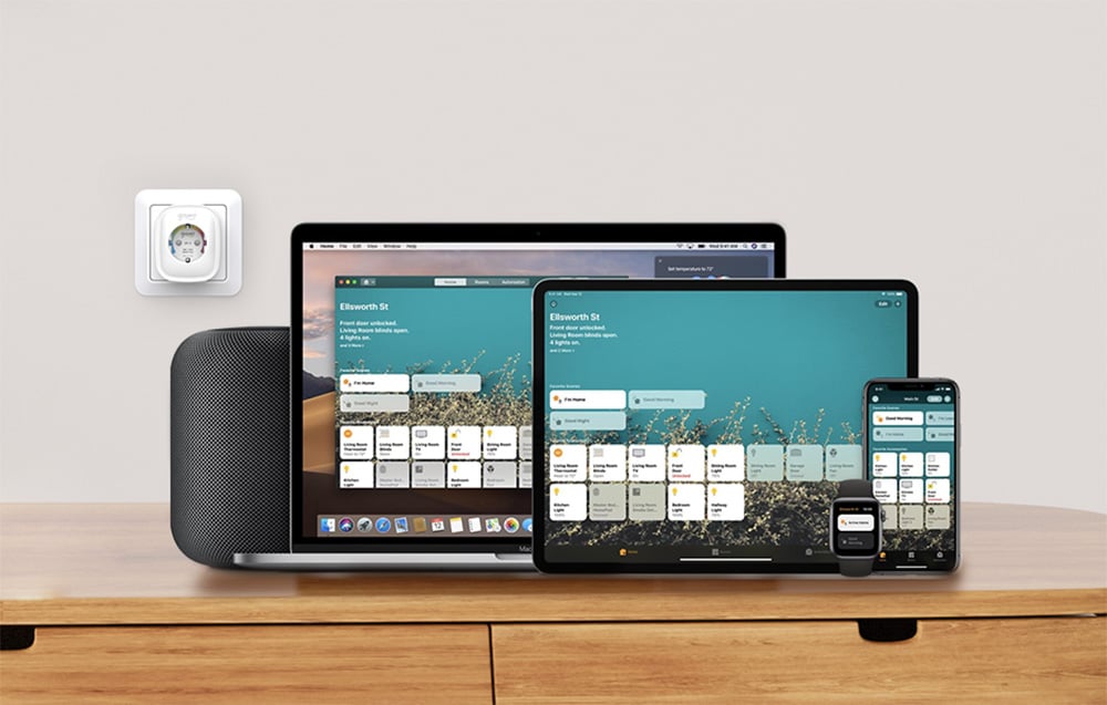 A smart outlet mounted on the wall next to a set of Apple devices, including a laptop, tablet, smartphone, watch and speaker running a home control app