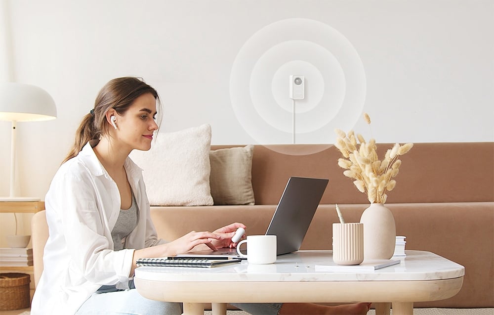 A woman working at a laptop, while a motion sensor with a graphic representation of the signal is visible on the wall in the background