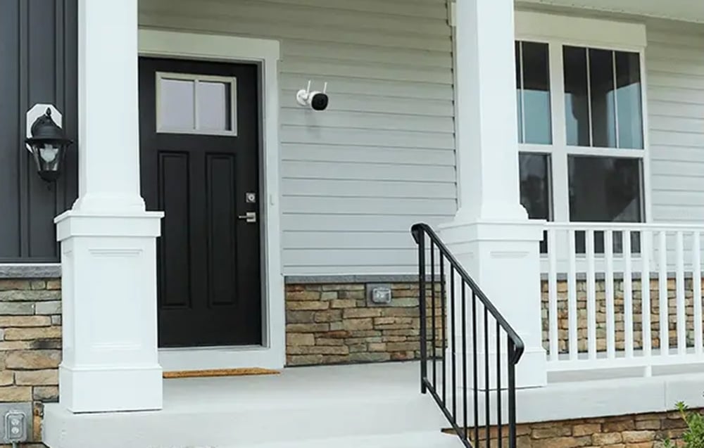 Entrance to a house with a black door and white pillars; a small black-and-white camera mounted above the door