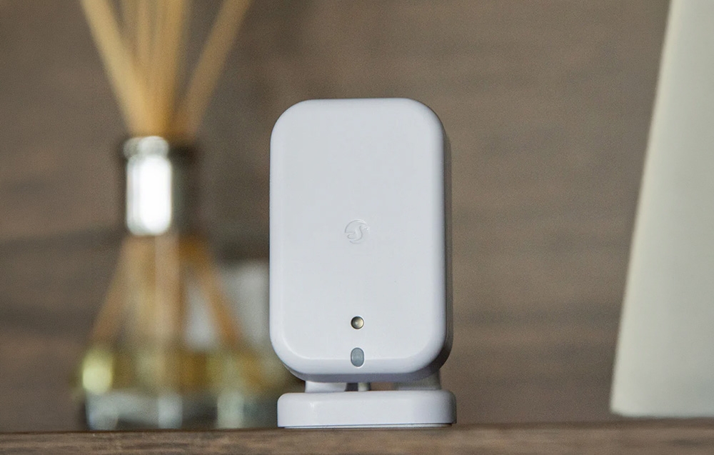 A white device standing on a wooden countertop, with a scent diffuser in the background
