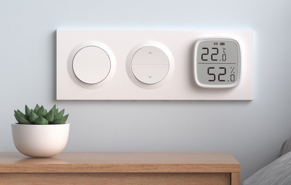 Triple frame for the switch on the wall. Next to it on a wooden table a green plant in a white pot.