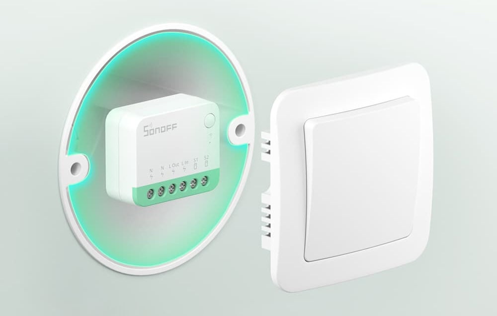 Sonoff switch in a wall box on a light-colored wall, next to the light switch