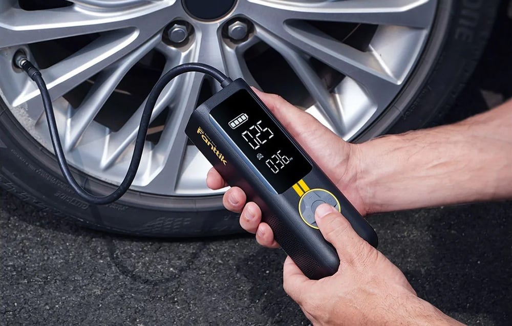A person holds a Fanttik mini compressor connected to the car's tire.