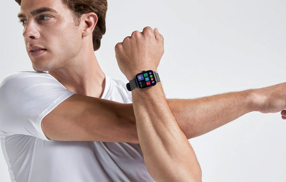 A man in a white T-shirt doing arm stretches with a black smartwatch on his wrist