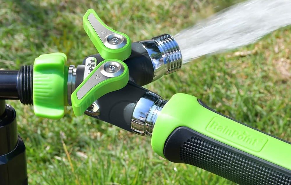 Two-way garden hose manifold with green valves and connected hose from which water flows