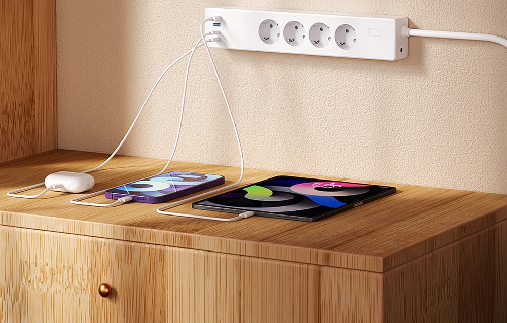 Power strip with connected headphones, smartphone and tablet lying on a light wood table top