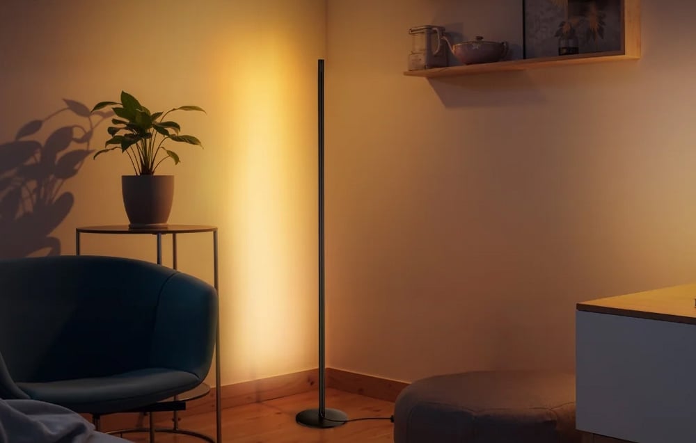 A lighting column casting a warm, yellow light onto the wall in a cozy room with an armchair and a plant.