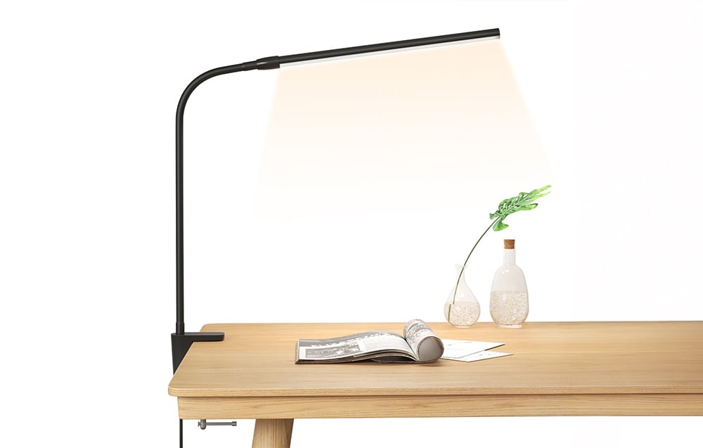A wooden side table with a lamp mounted on the side, illuminating an open magazine and two vases with plants.