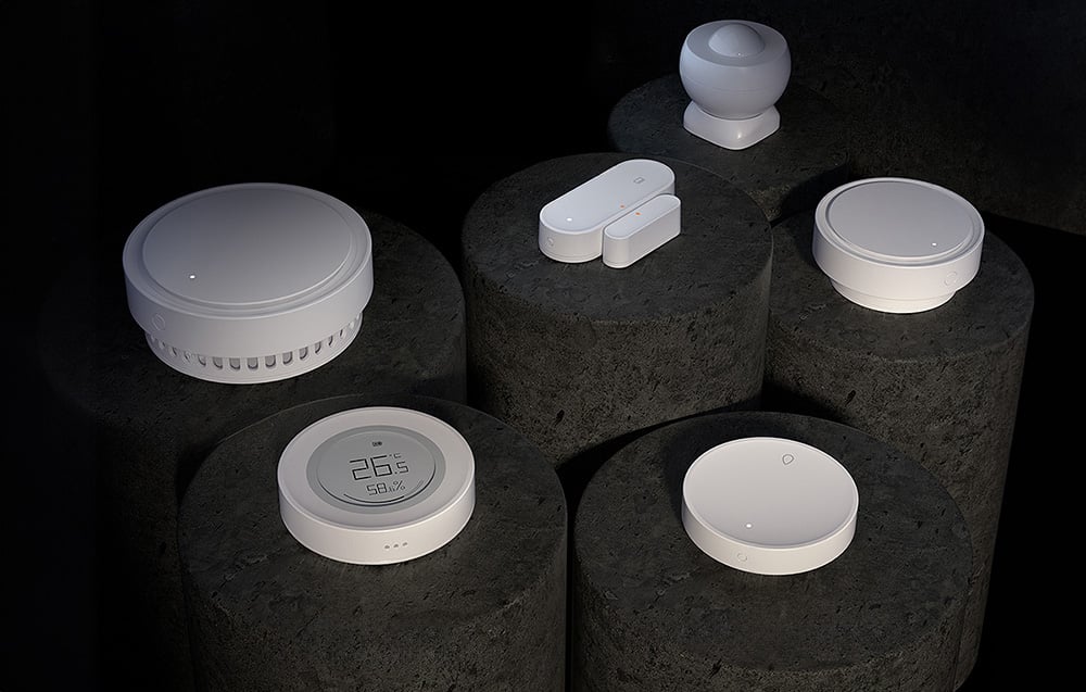 A set of six white smart home devices on black cylindrical pedestals, including a motion sensor, an opening sensor and more