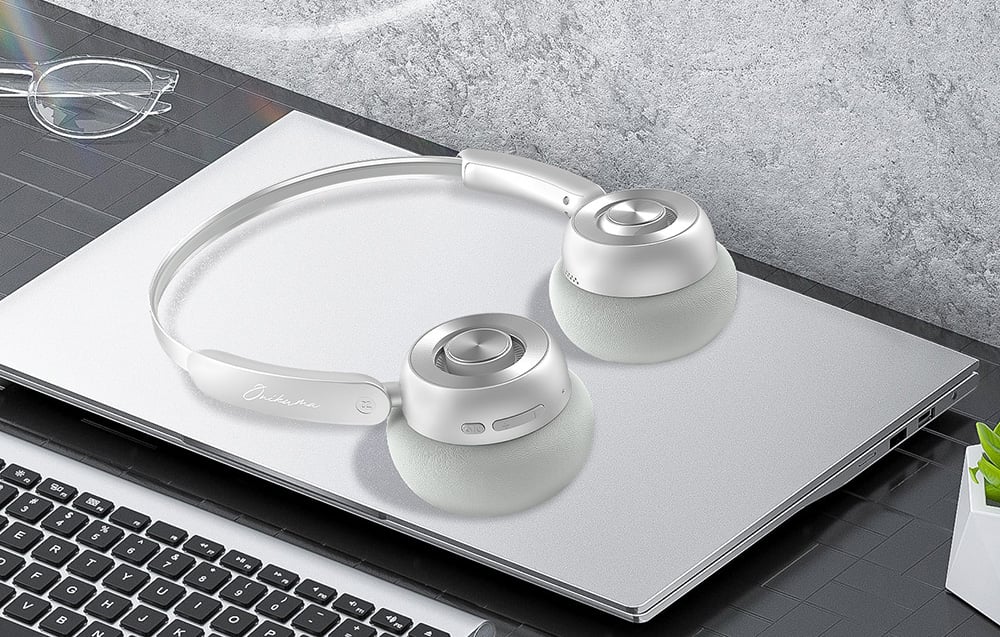 Onikuma headphones lying on a closed laptop, next to it you can see the glasses and keyboard of another laptop