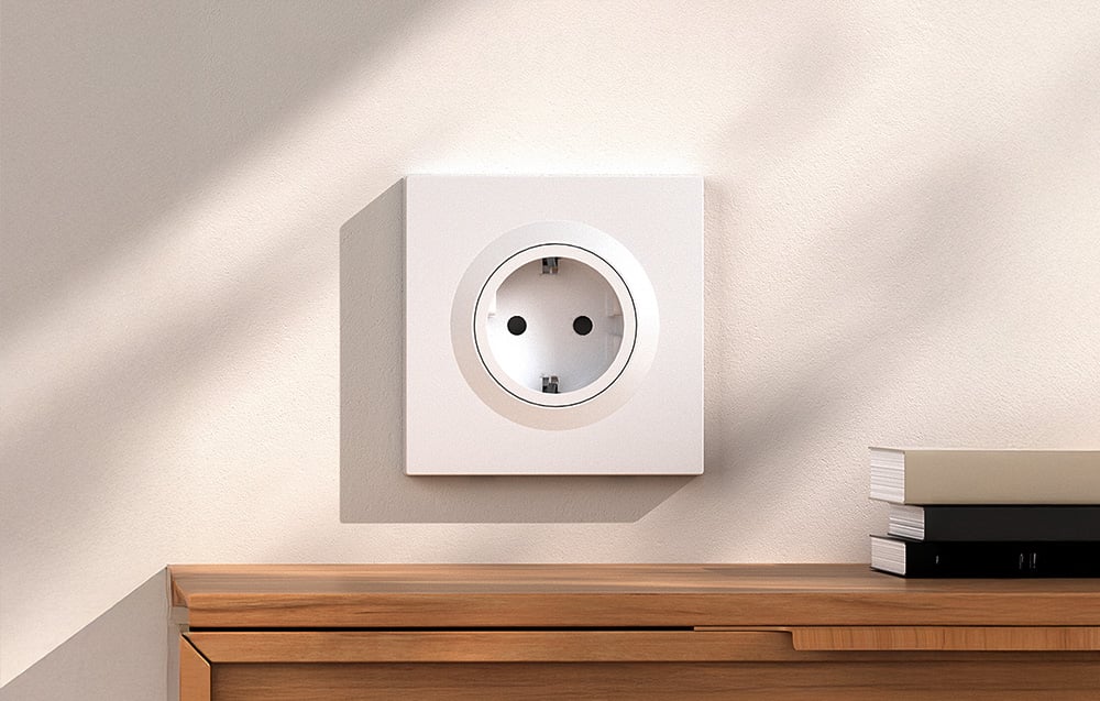 A white traditional wall socket mounted above a wooden dresser in a bright room
