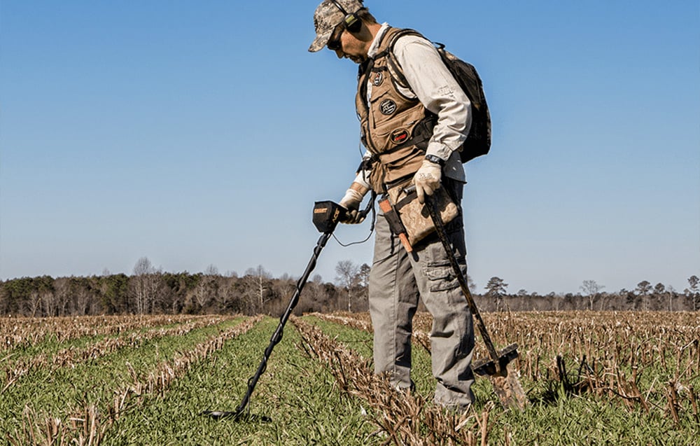 A man with a metal detector searches a field.