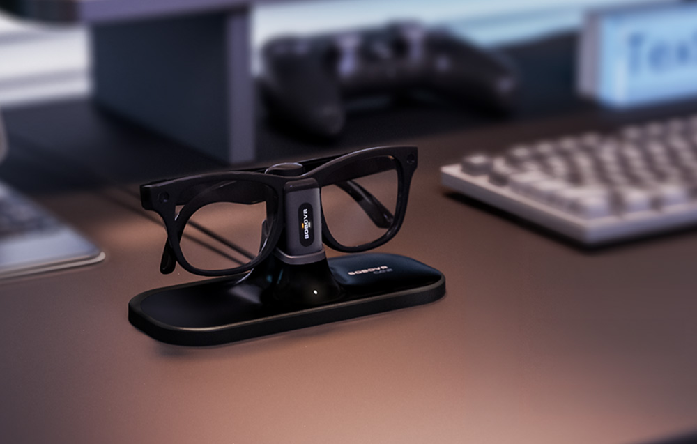 Smart glasses placed on the elegant BOBOVR CG2 docking station on a desk next to a keyboard and electronic devices.