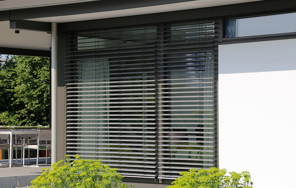 Modern building with large windows and external horizontal blinds in aluminum frame, green in the background