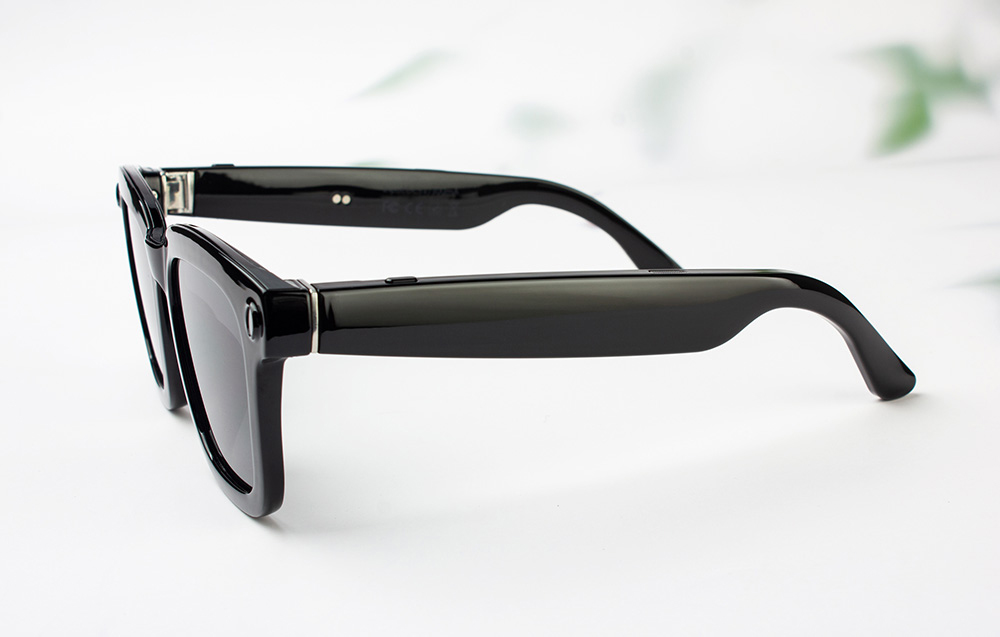 Close-up of the side of black, shiny smart glasses frames lying on a light background.