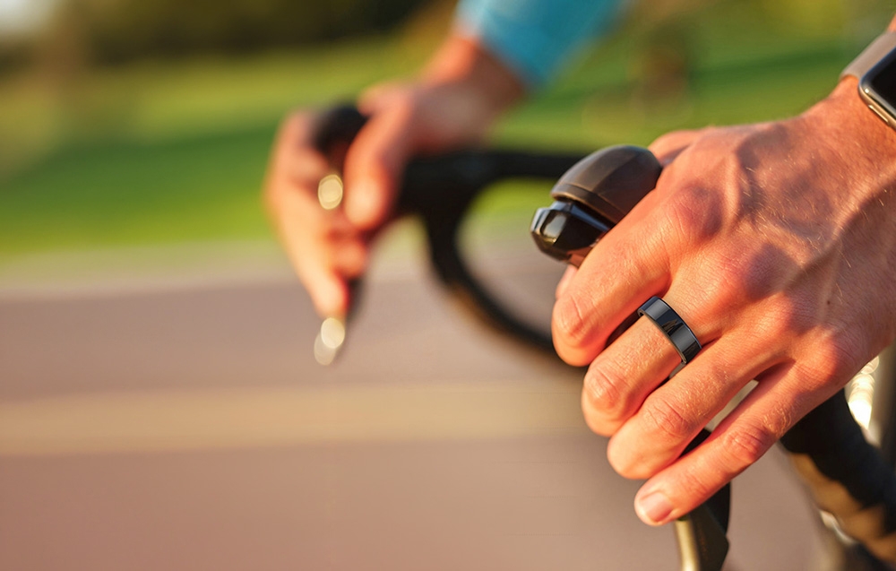 A cyclist’s hands on black handlebars with a dark smart ring visible on his finger