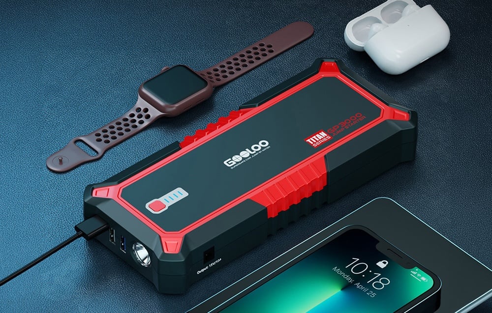 Car jump starter next to a smartwatch, headphones, and a phone