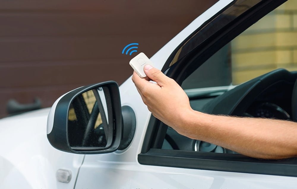 Hand holding garage door remote control at car window with signal symbol