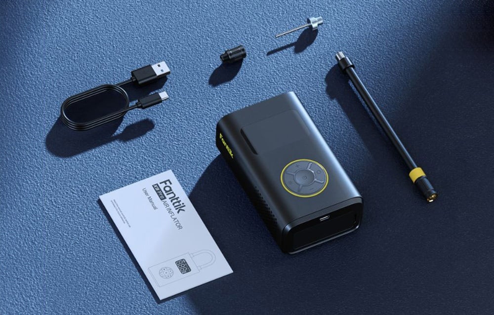 The mini compressor with a set of accessories lies on a dark blue surface.