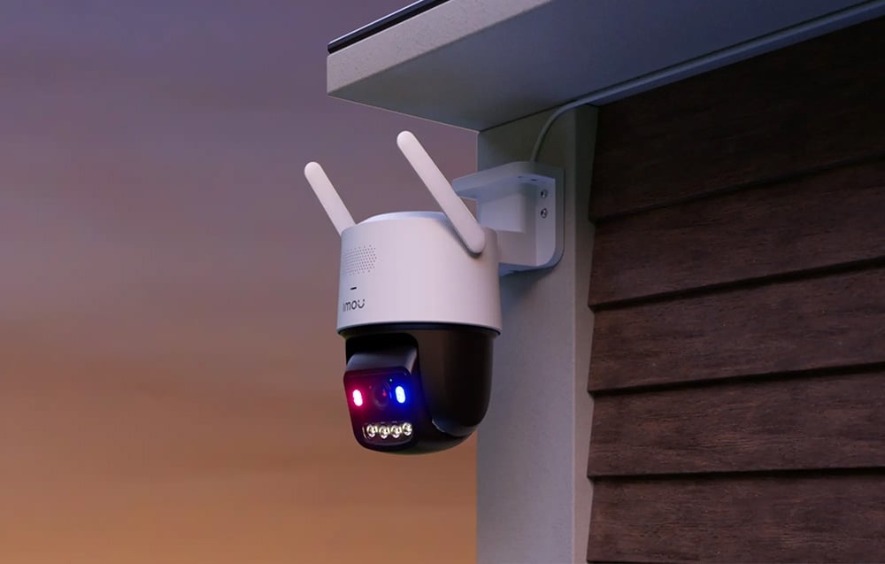 PTZ camera under a roof overhang after dark; two LEDs are lit on the device: red and blue