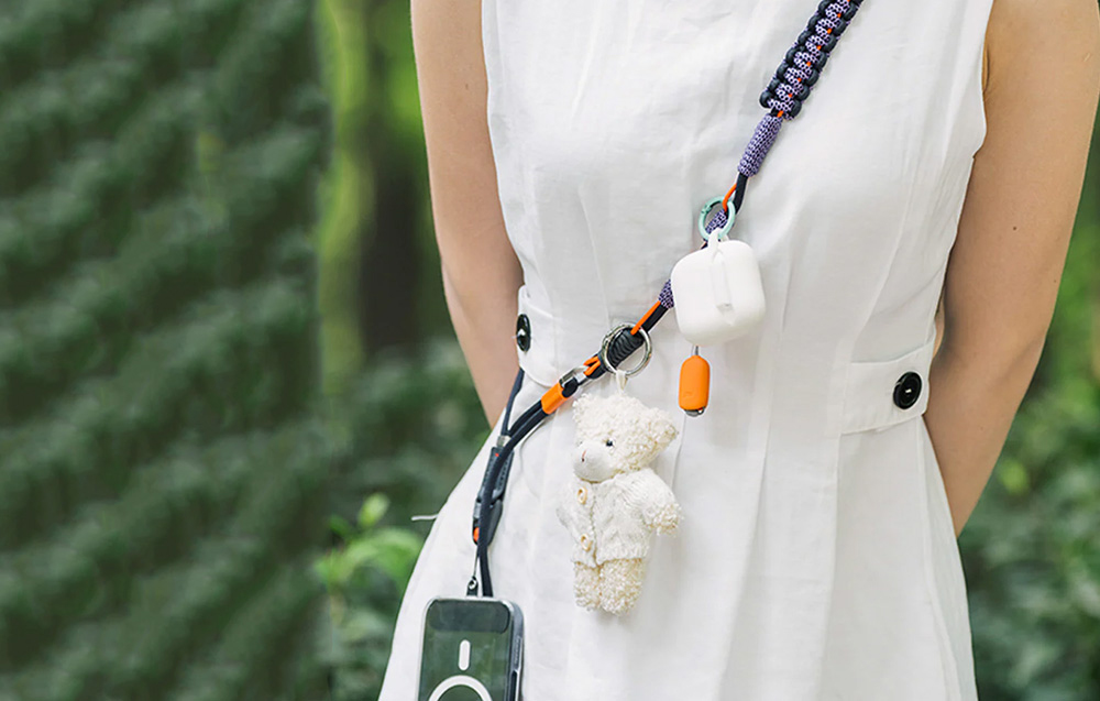 Woman in white dress wears a strap slung over her shoulder to which accessories and smartphone are mounted