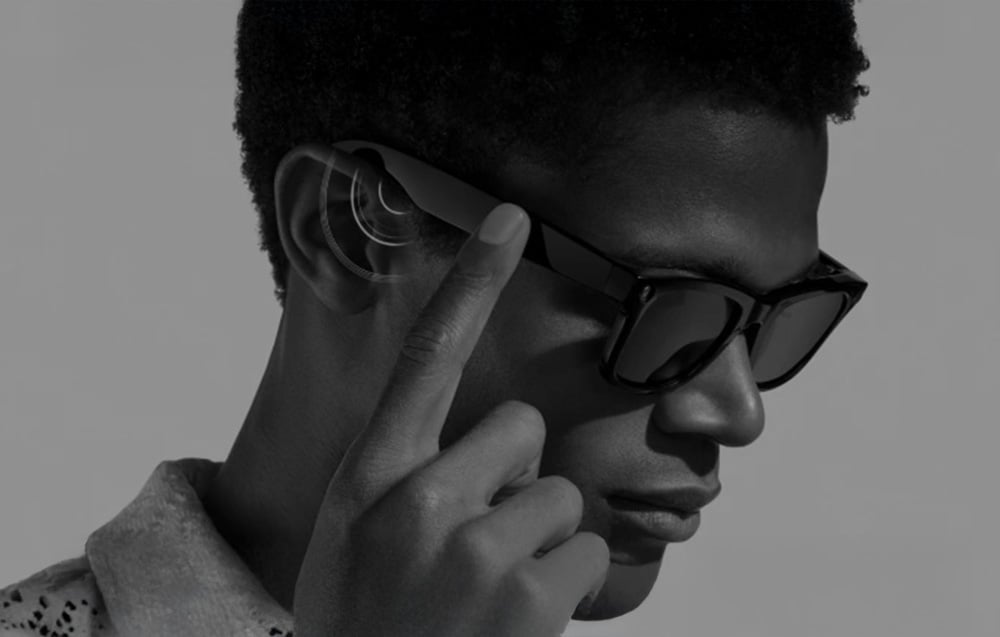 Black-and-white photo of a man wearing AI glasses, touching the frame with his finger