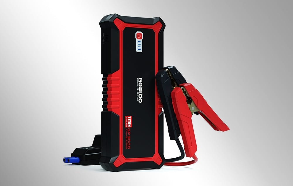 Portable car jump starter with connected clamps on a light background