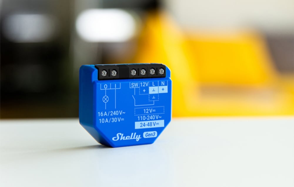 The blue Shelly Gen3 module stands on a white surface, with technical markings clearly visible