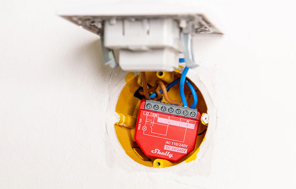 Shelly module mounted in open wall box with wiring visible and switch cover partially offset